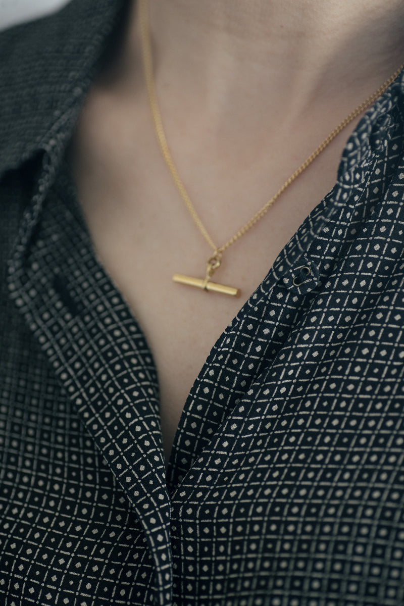 Charlotte 18K gold plated stainless steel necklace with bar pendant on a soft gray background