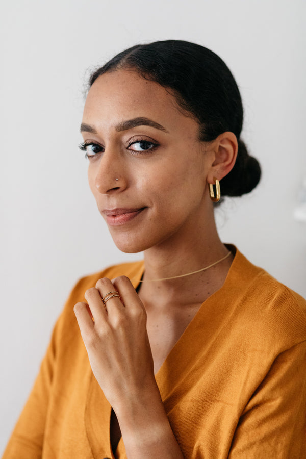 Pair of Sibylle 18k gold plated elongated loop earrings on dark fabric background