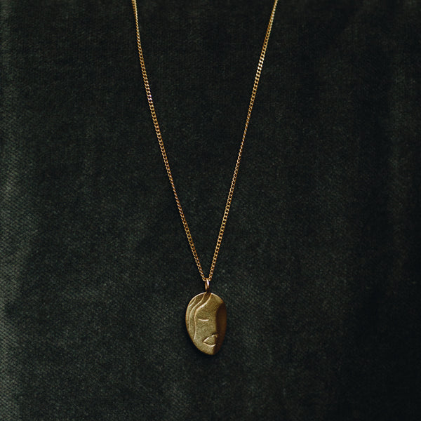 Le Visage 18k gold plated portrait necklace with abstract face design on dark background