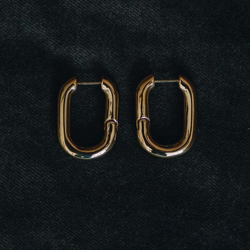 Pair of Sibylle 18k gold plated elongated loop earrings on dark fabric background