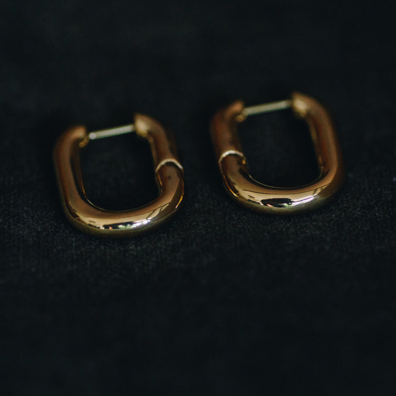 Pair of Sibylle 18k gold plated elongated loop earrings on dark fabric background