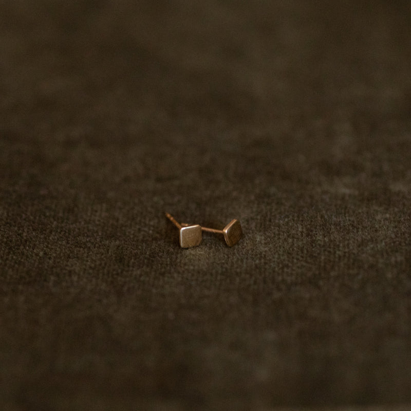 Pair of 14k solid gold square mini stud earrings on brown leather background