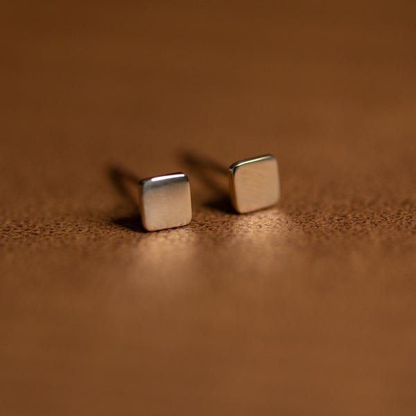 Pair of 14k solid gold square mini stud earrings on brown leather background