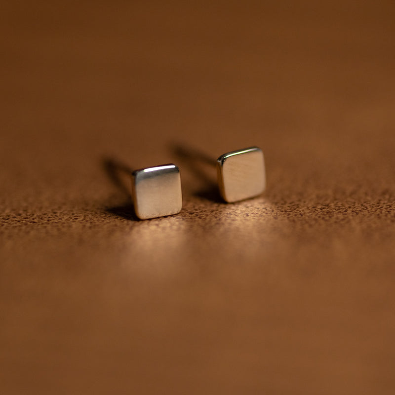 Pair of 14k solid gold square mini stud earrings on brown leather background